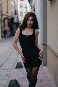 Young woman posing in a fashionable black dress on a narrow İstanbul street, captured in a candid urban setting.