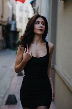 Charming woman in black dress strolling through an İstanbul alley, reflecting modern fashion.