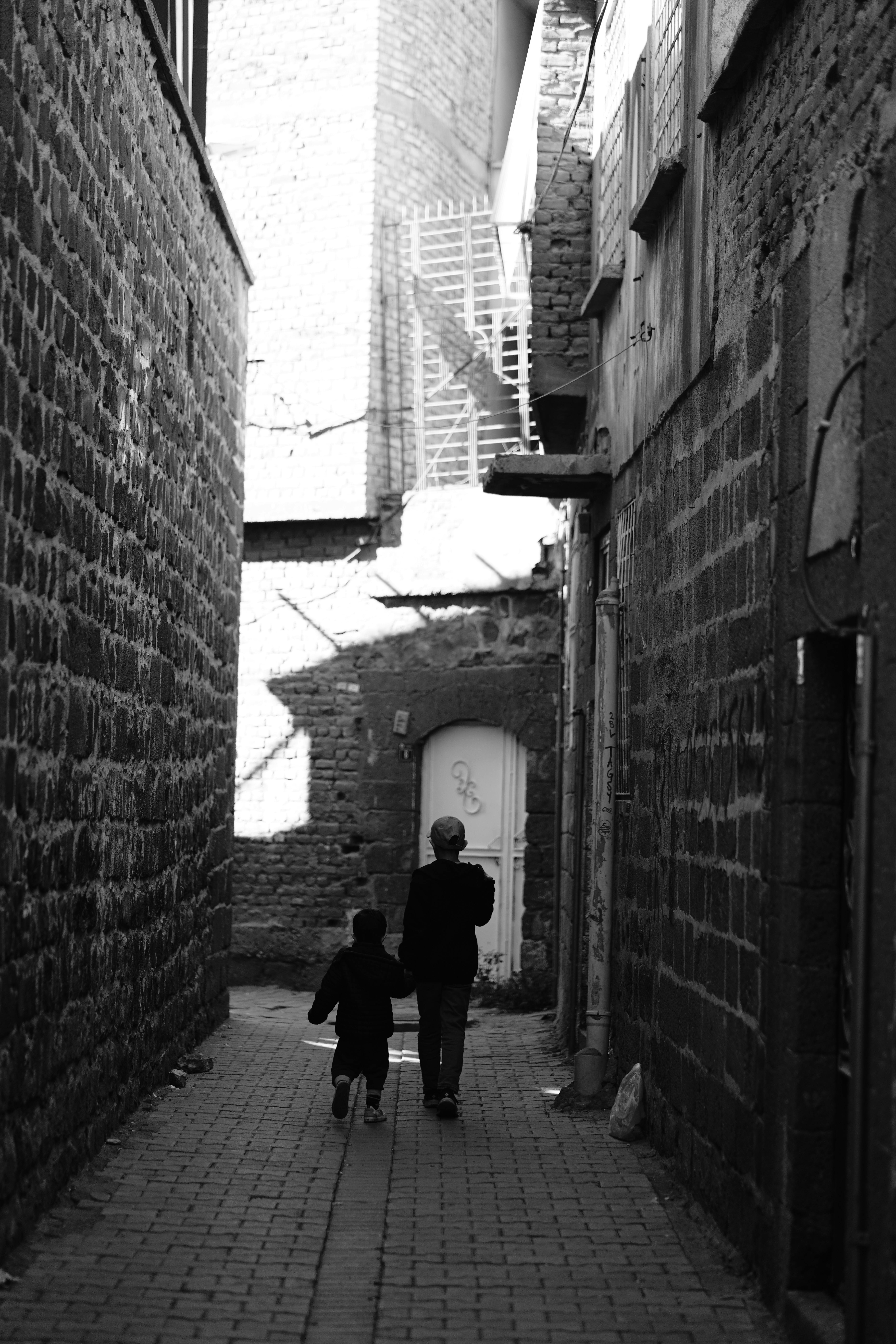 Monochrome alley scene with two people walking away, urban shadows.