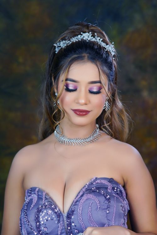 Free Portrait of a woman in a glamorous purple evening gown with elegant jewelry against a studio backdrop. Stock Photo