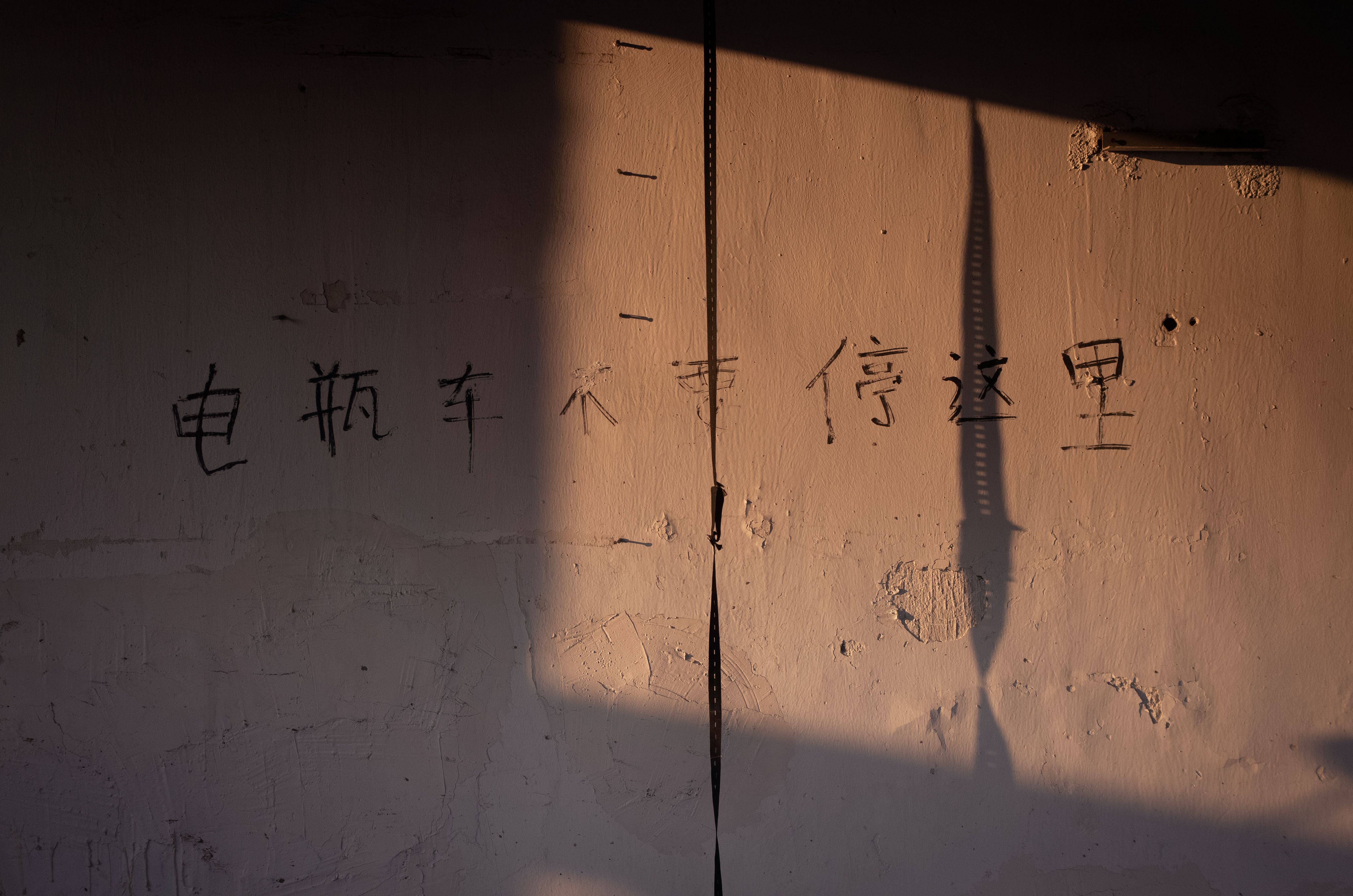 Sunlit wall with Chinese characters and shadow play creating a dramatic effect.