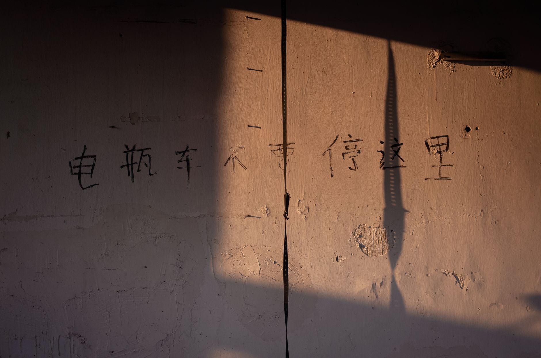 Sunlit wall with Chinese characters and shadow play creating a dramatic effect.