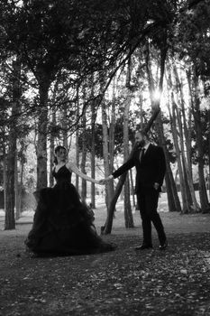 A stylish couple holding hands in a forest, captured in black and white.