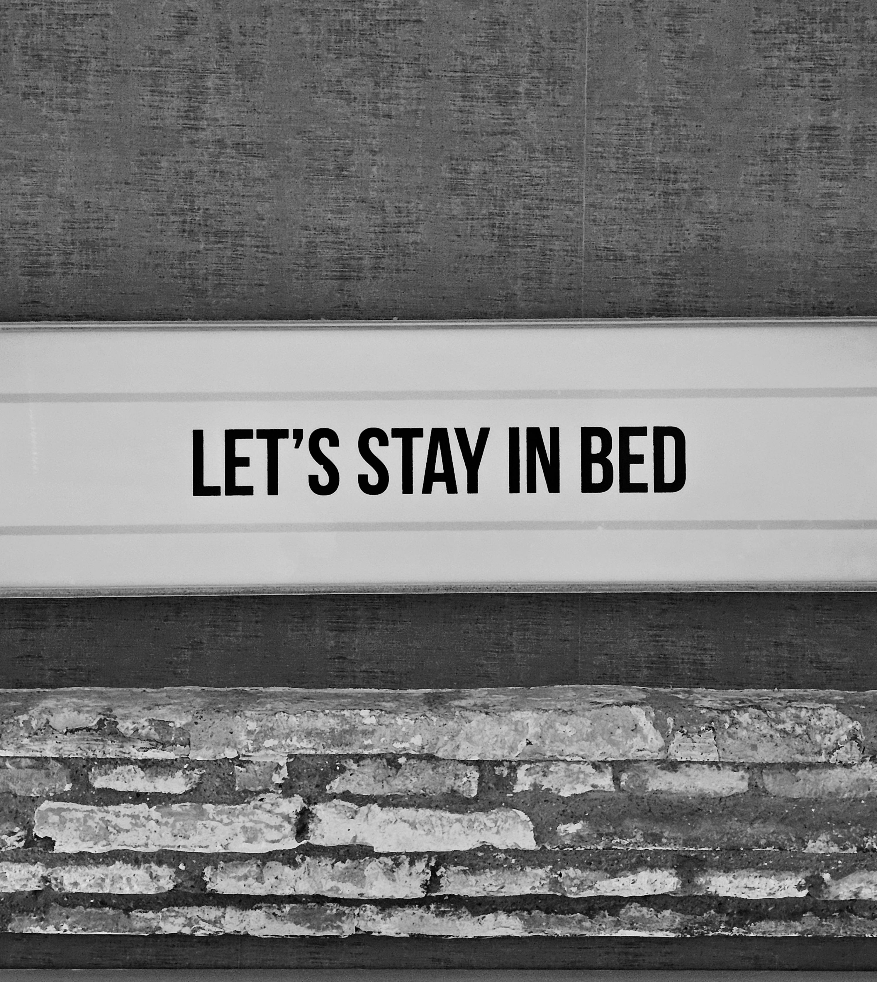 Black and white photo of a sign with the text "LET'S STAY IN BED."