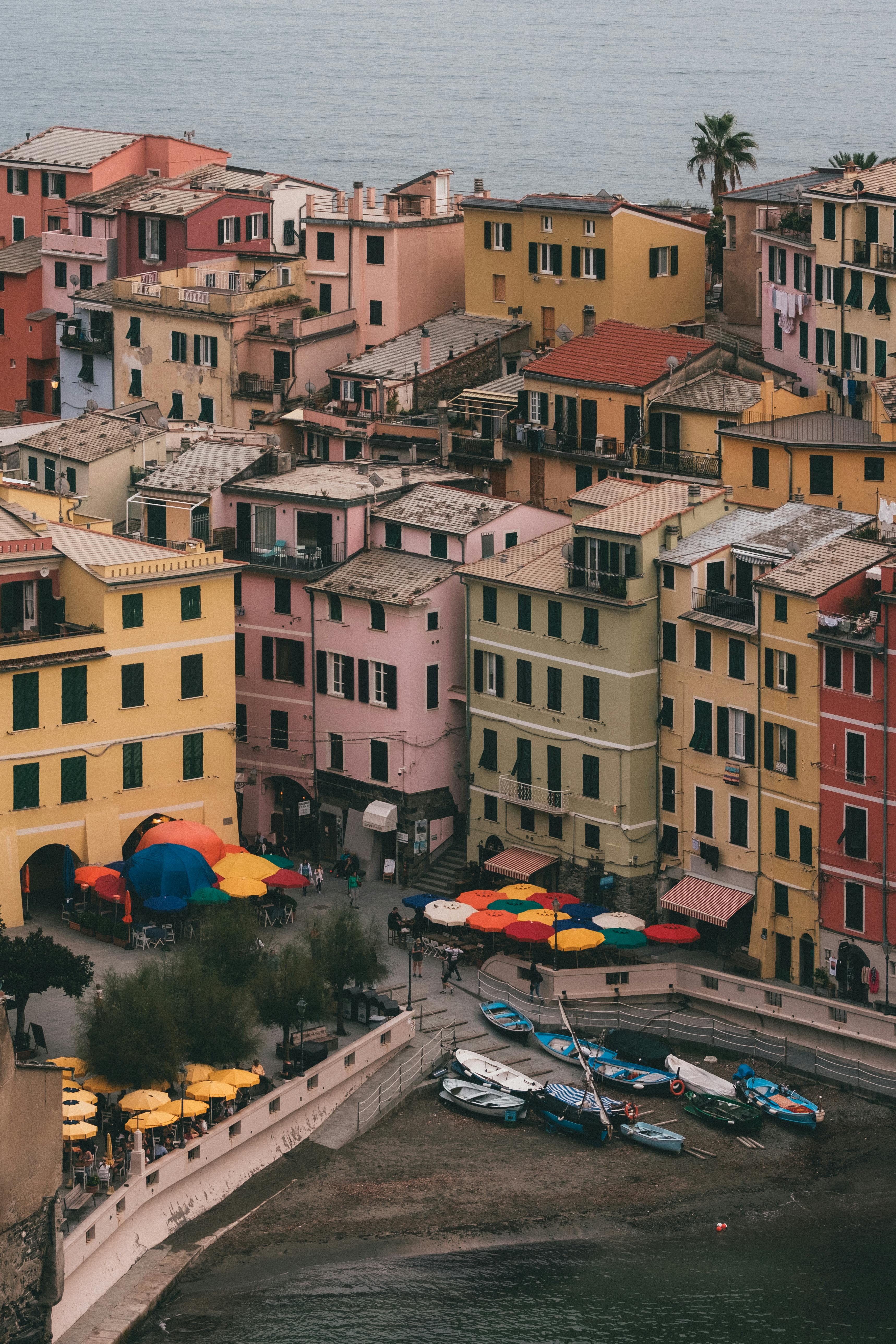 Vibrant buildings line the harbor of Vernazza, Italy with colorful umbrellas and boats below.