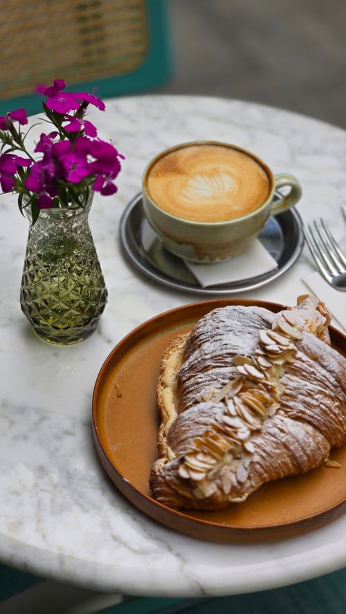 Free Almond croissant and latte on café table with flowers. Stock Photo