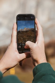 Person photographing mountains with a smartphone in the Italian Alps.