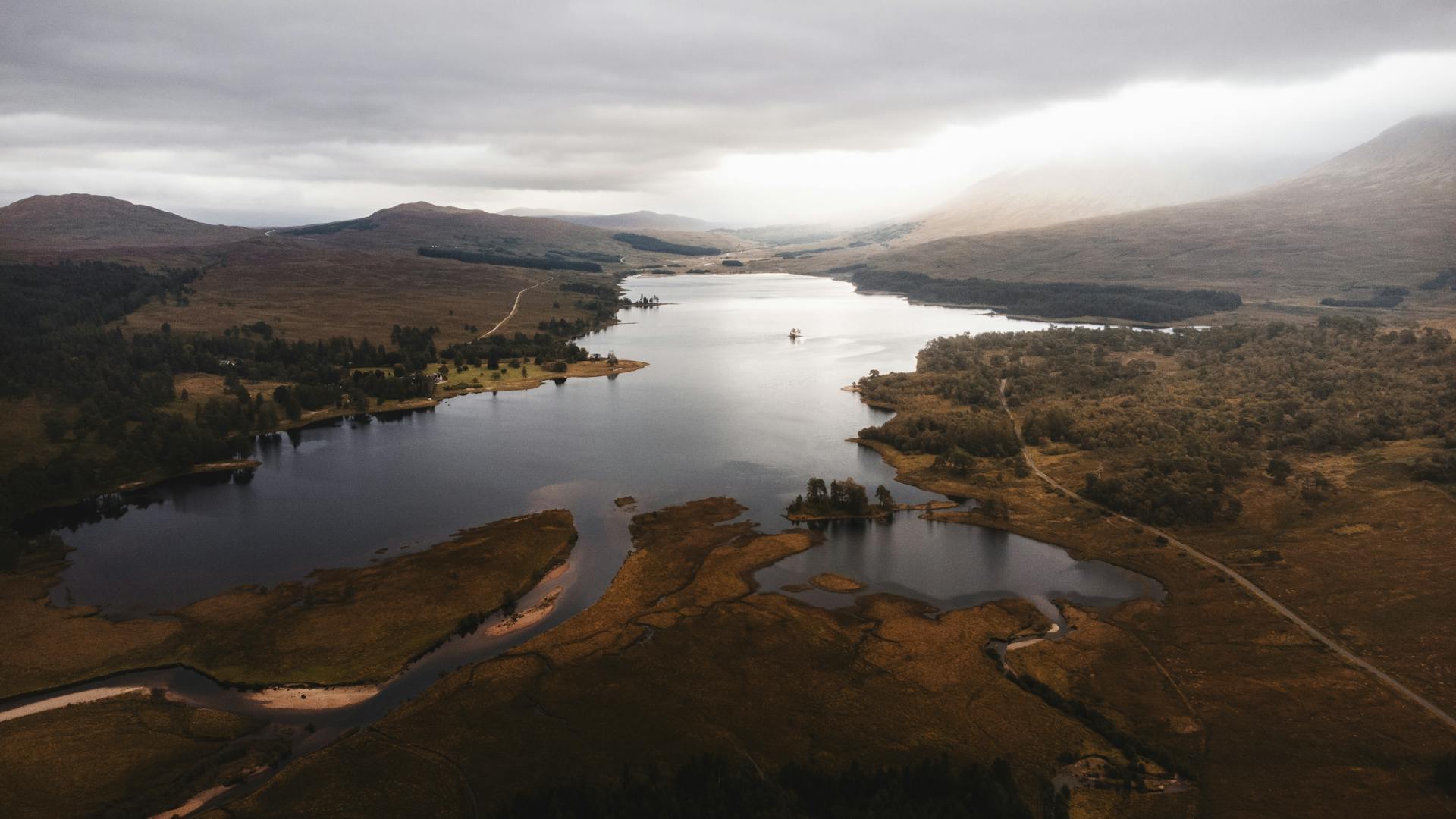 A dramatic aerial view of a loch surrounded by mountainous landscape in the Scottish Highlands.