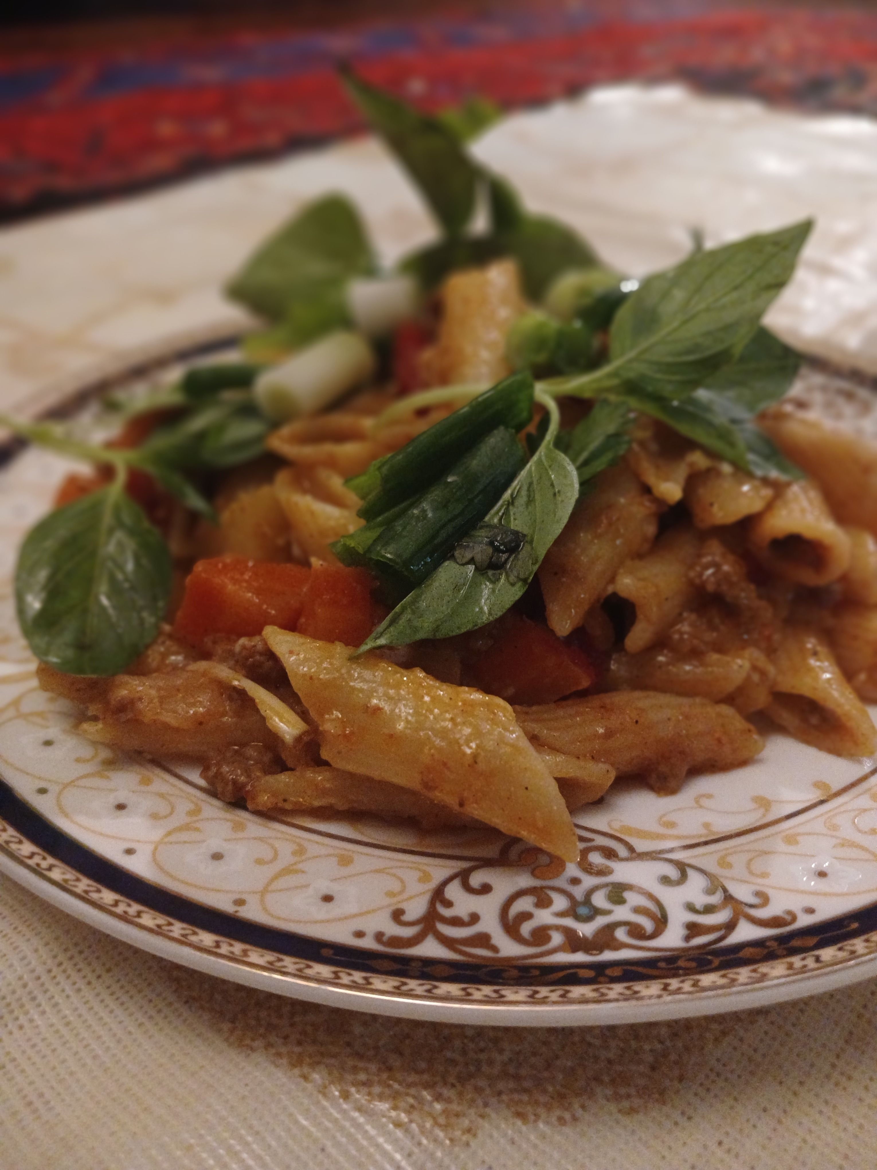 Close-up of penne pasta with fresh herbs on a decorative plate.