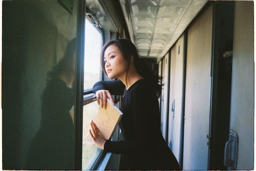 Free Woman gazing out train window, holding book in quiet reflection. Stock Photo