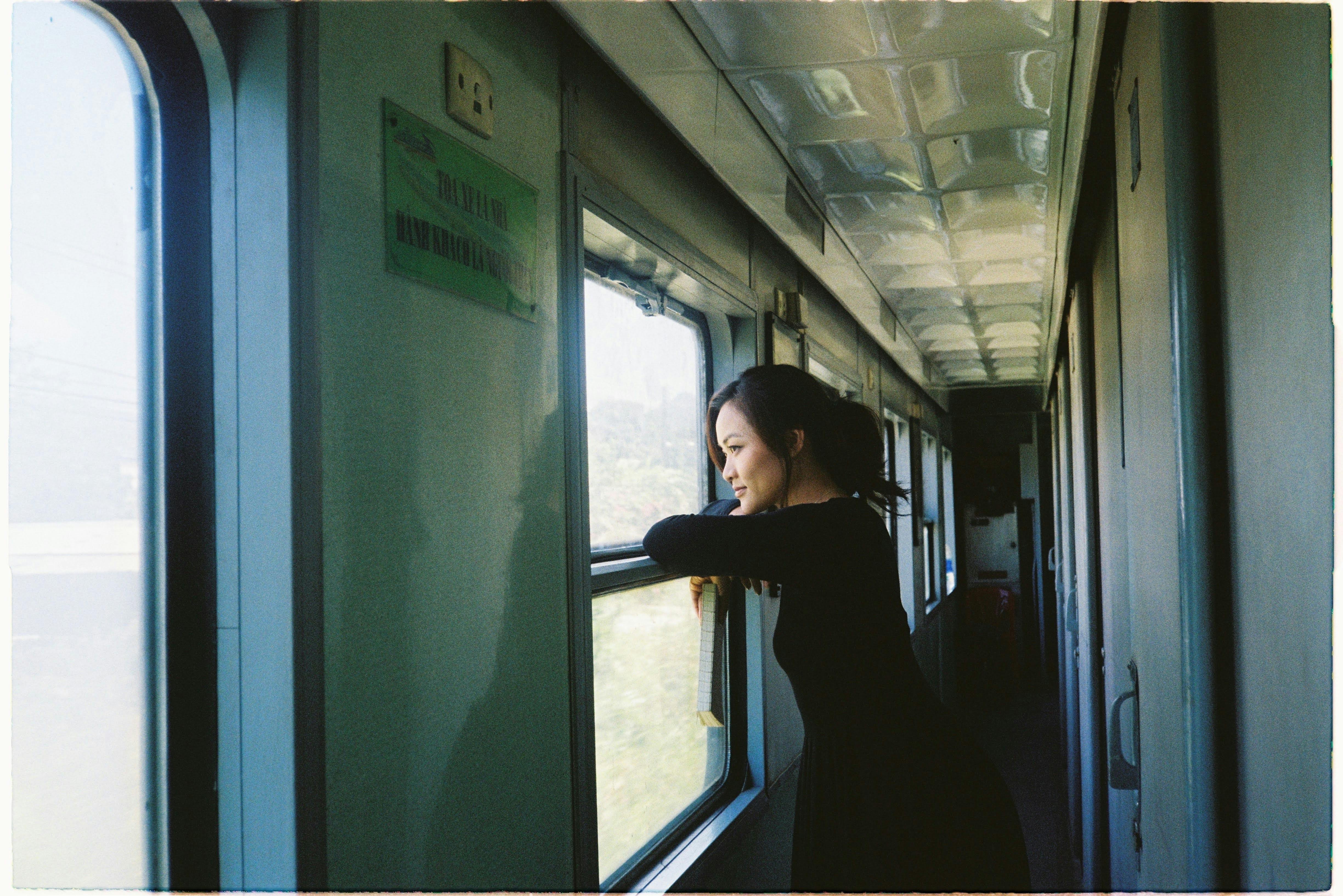 A woman looks outside the train window during a scenic daytime journey, capturing a moment of reflection.