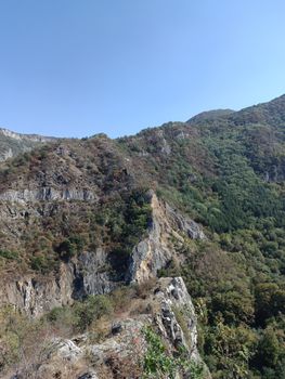 Breathtaking view of rugged mountain landscape with clear blue sky, lush greenery, and rocky formations.