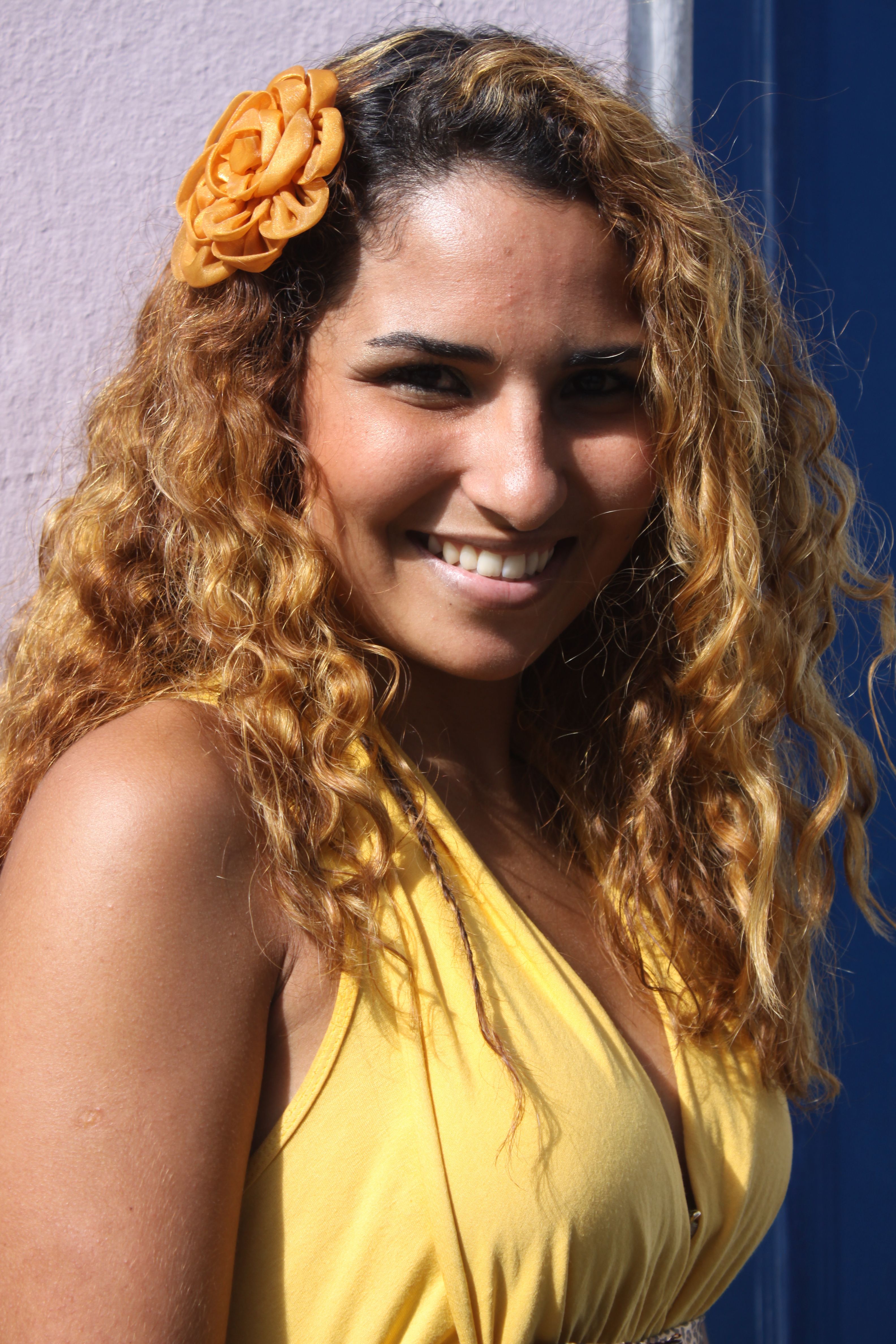 Cheerful adult woman with curly hair and flower clip, posing outdoors in Salvador.