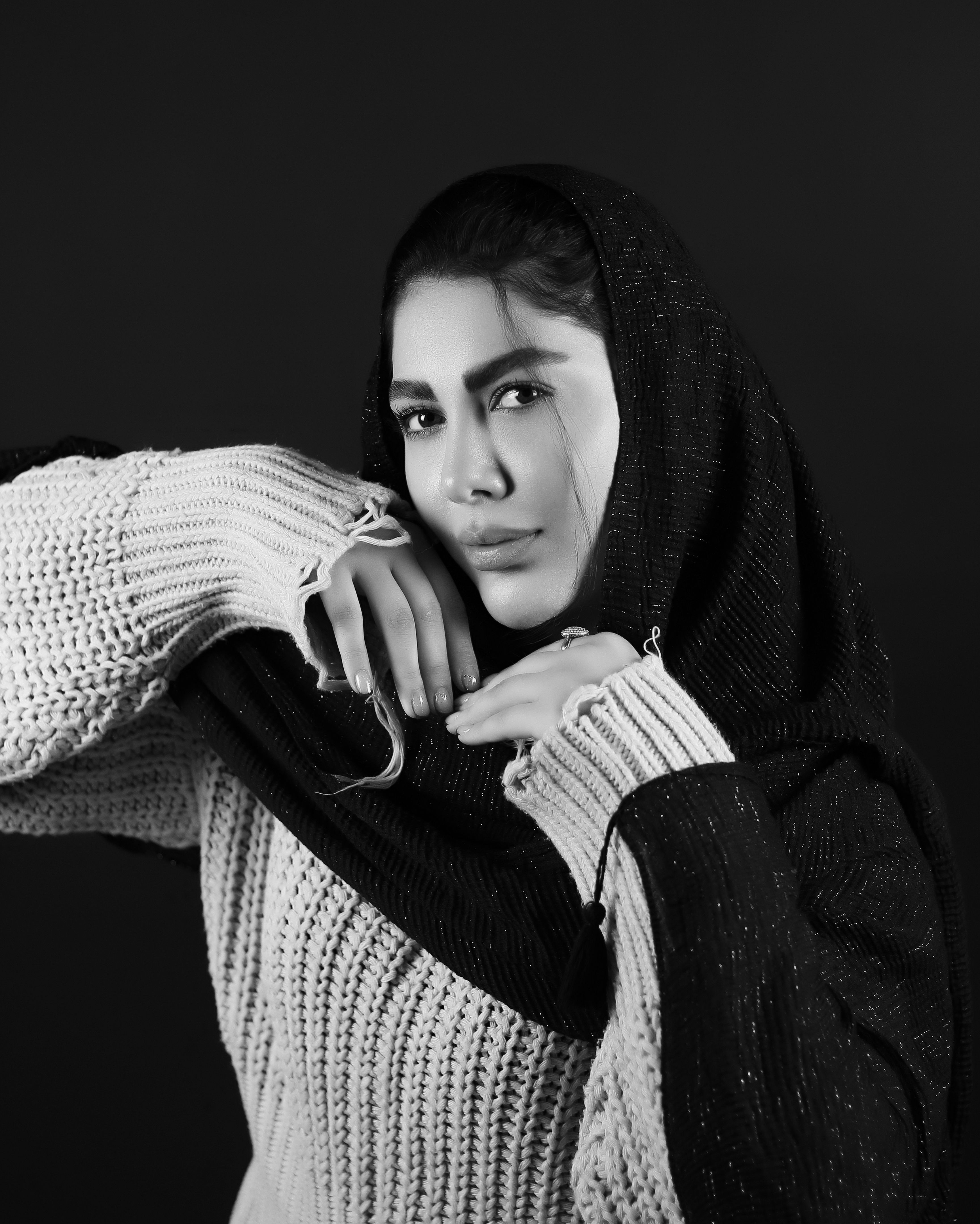 Artistic black and white portrait of a woman in a sweater and scarf, striking a thoughtful pose.