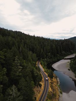 Aerial view of a winding road through California's Redwood National Park with lush green trees.