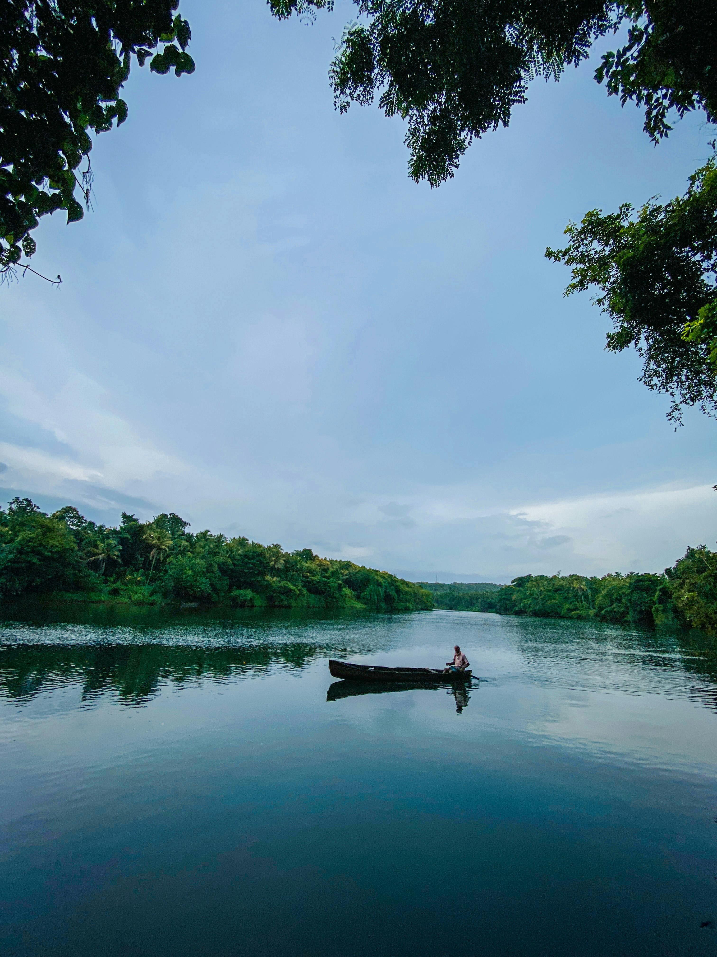 Gratis Vista tranquilla di una barca solitaria su un rigoglioso corso d'acqua nel Kerala, in India. Foto a disposizione