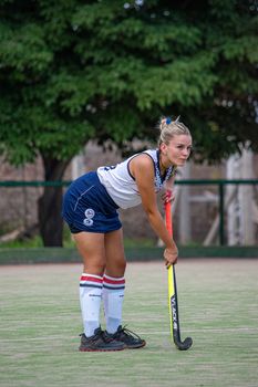 Focused female field hockey player preparing on grassy outdoor pitch.