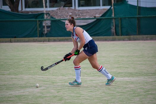 Focused female field hockey player in action during a game outdoors.
