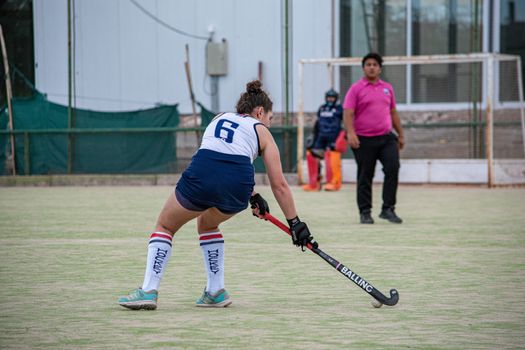 Female field hockey player in action, dribbling on a green outdoor field during a match.