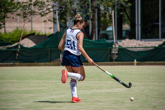 Athletic woman playing field hockey on sunny day, showcasing action and sports spirit.