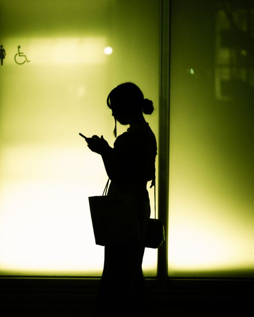 Free Silhouette of a woman using smartphone against a green lit wall in Tokyo, Japan at night. Stock Photo