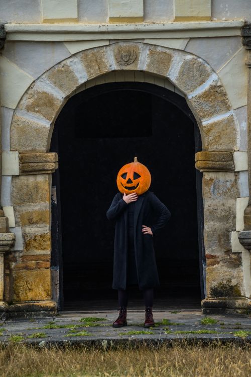 Free A figure with a pumpkin head stands in an old archway, setting a mysterious Halloween vibe. Stock Photo
