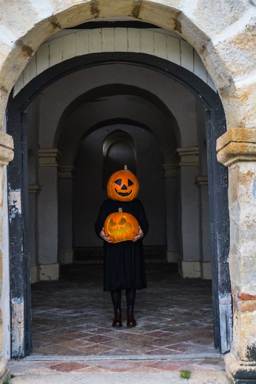 Free Mysterious figure with pumpkin head holding carved pumpkin in old archway. Stock Photo