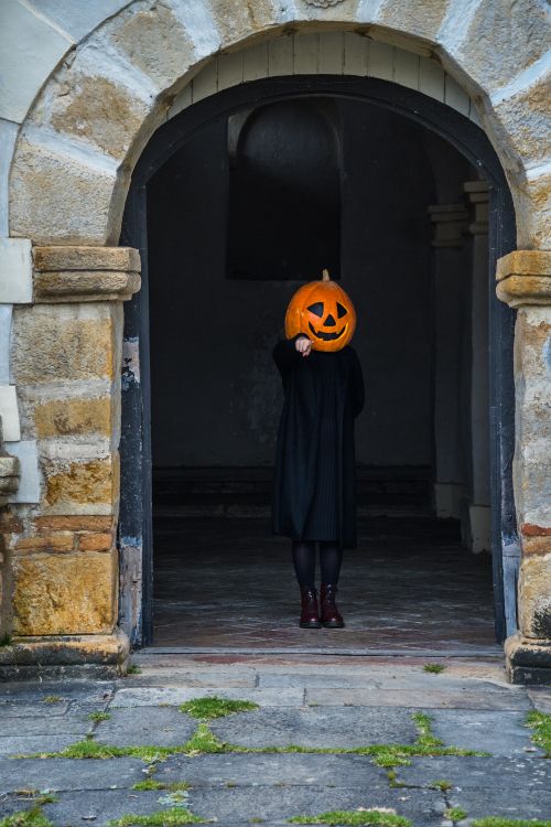 Free Person with pumpkin head costume stands in an ancient stone archway, conveying a spooky Halloween vibe. Stock Photo
