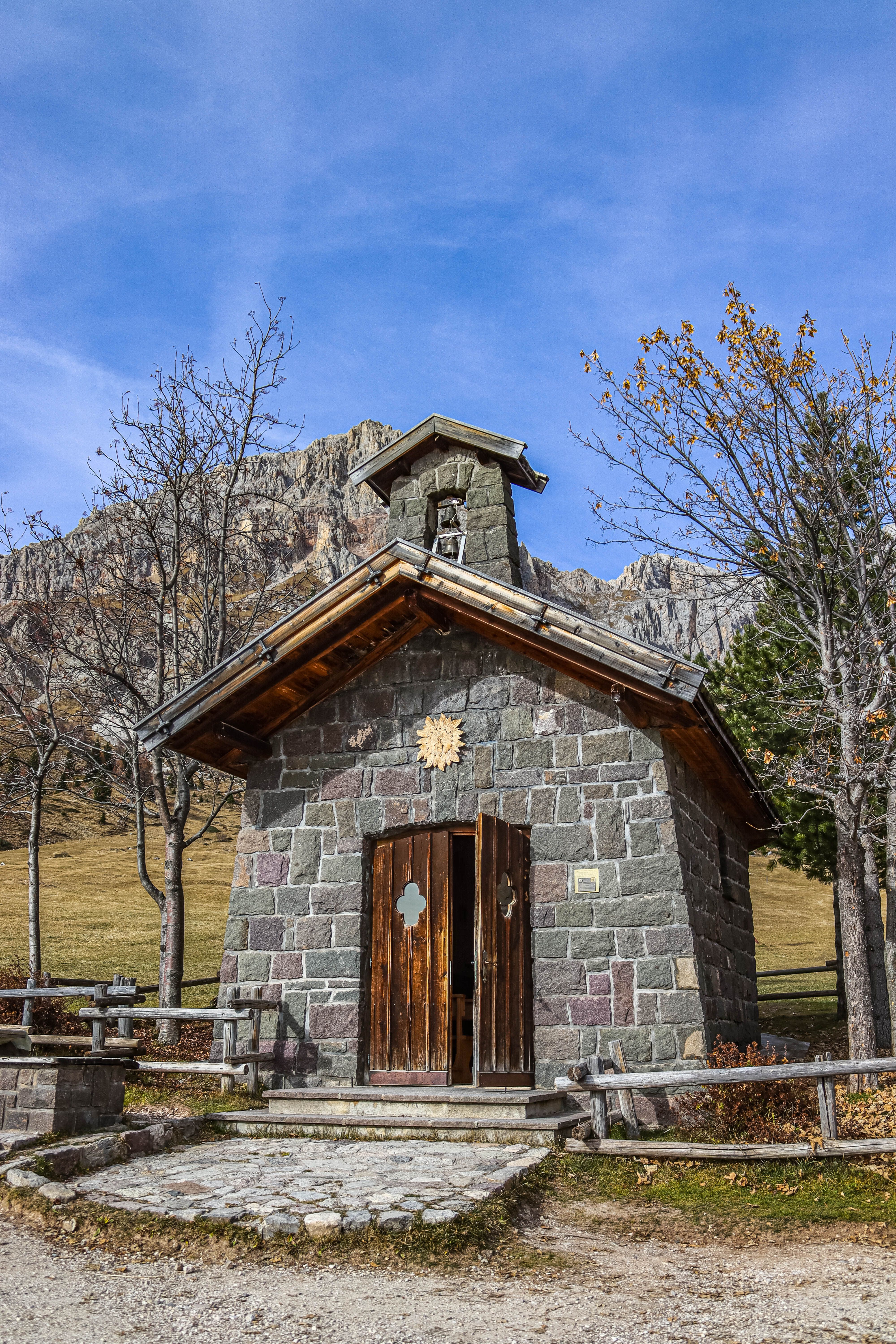 Fotomural Encantadora pequeña capilla de piedra situada con un impresionante telón de fondo montañoso bajo un cielo azul claro.