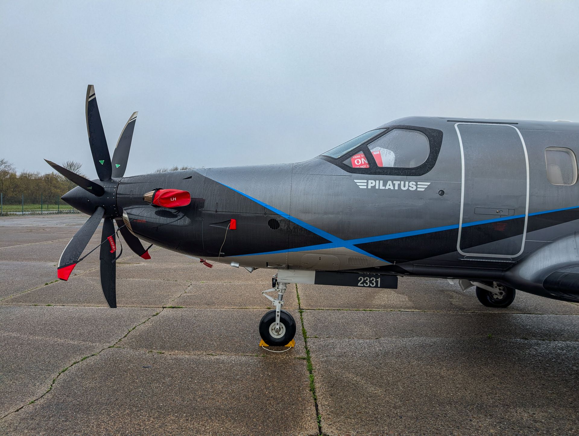 Close-up of a Pilatus aircraft parked on a wet runway, showcasing sleek design and aircraft details.