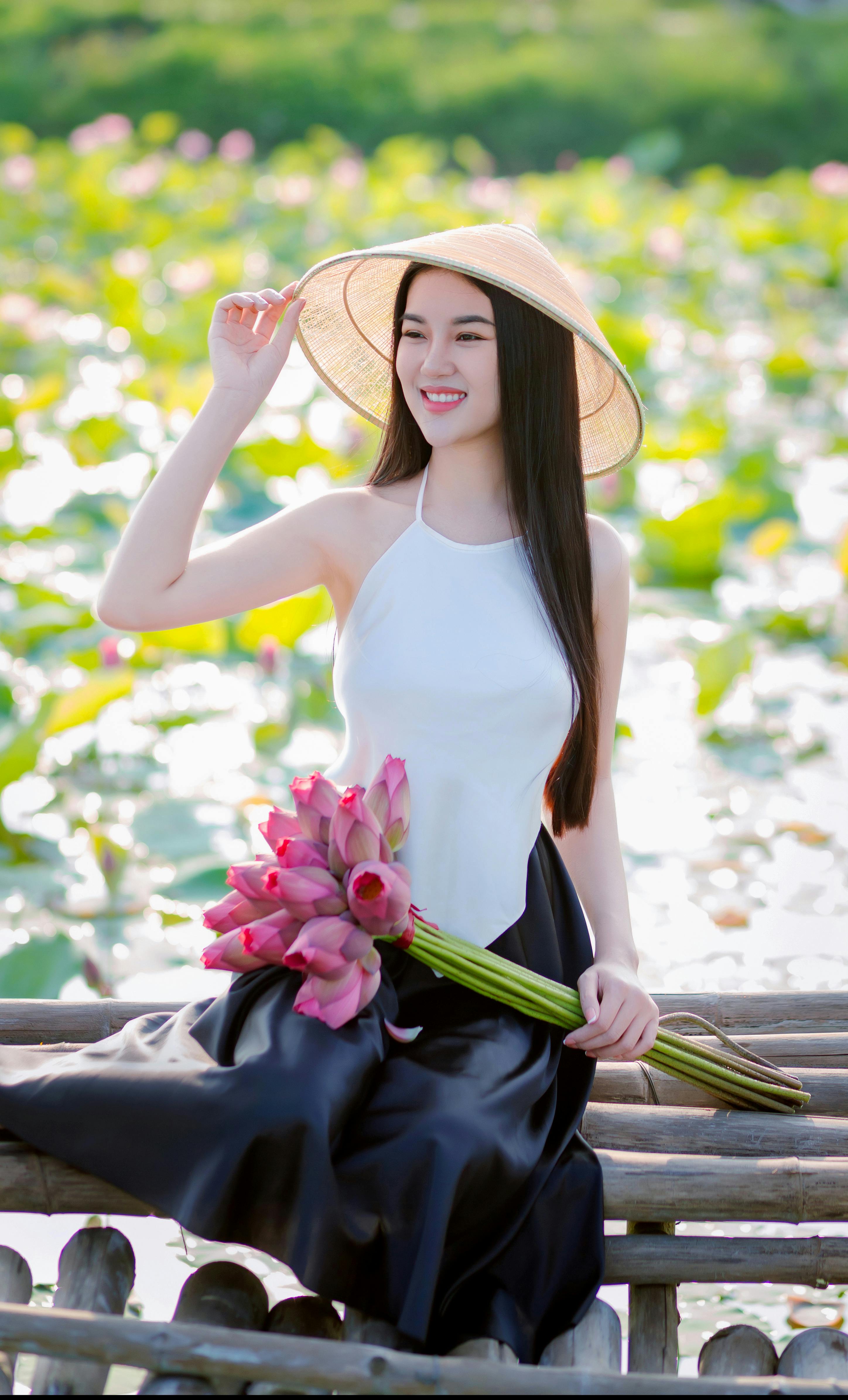 A young woman in traditional attire posing with lotus flowers in a vibrant pond in Hoi An.