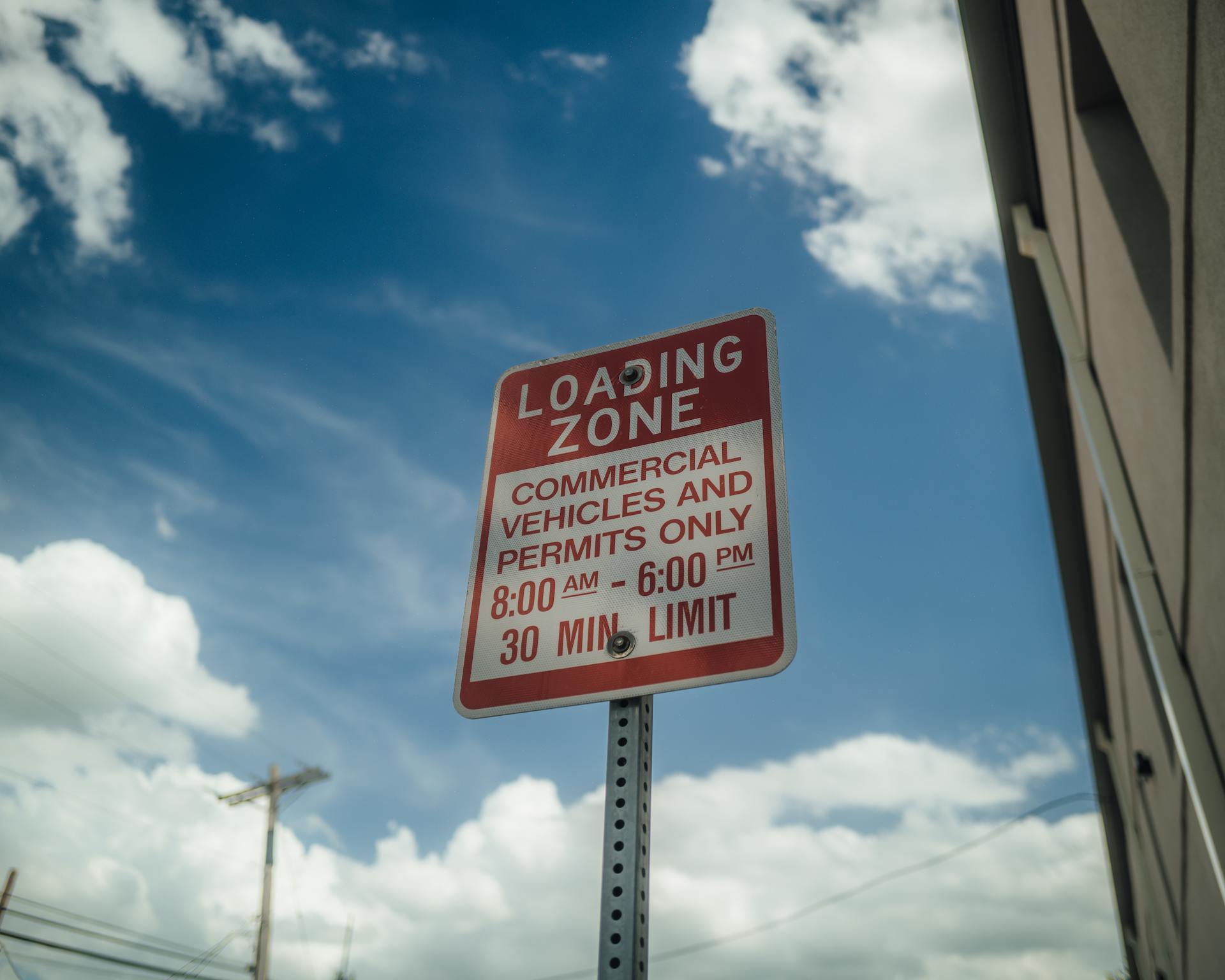 Red and white loading zone sign indicating time restrictions against a bright blue sky.