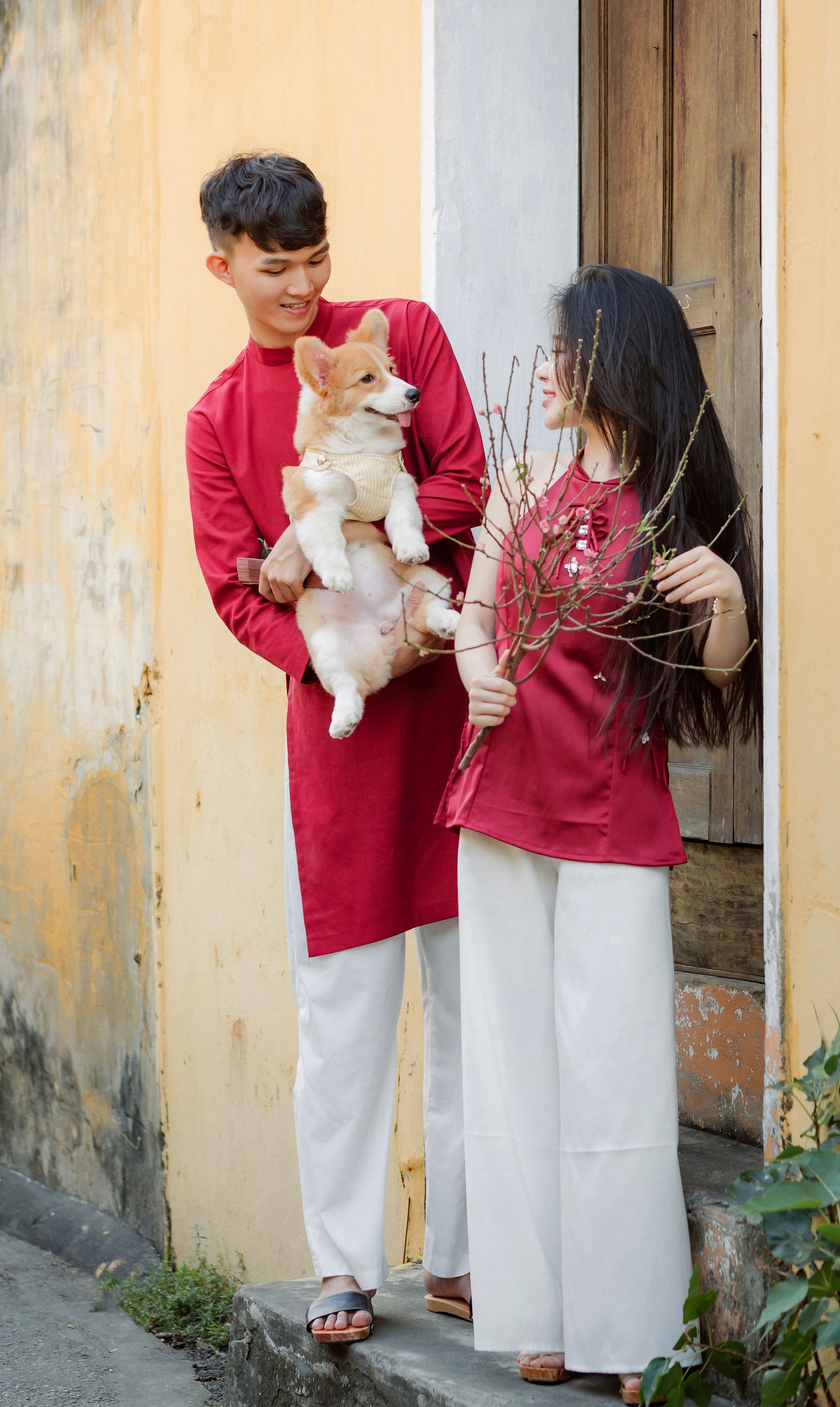 A couple in traditional attire holding a corgi dog, captured in Hội An, Vietnam.
