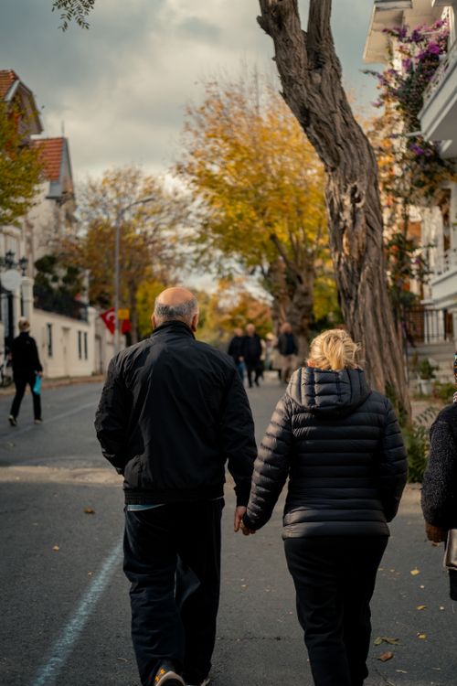 Free An older couple strolls arm in arm on a charming street amidst fall foliage. Stock Photo