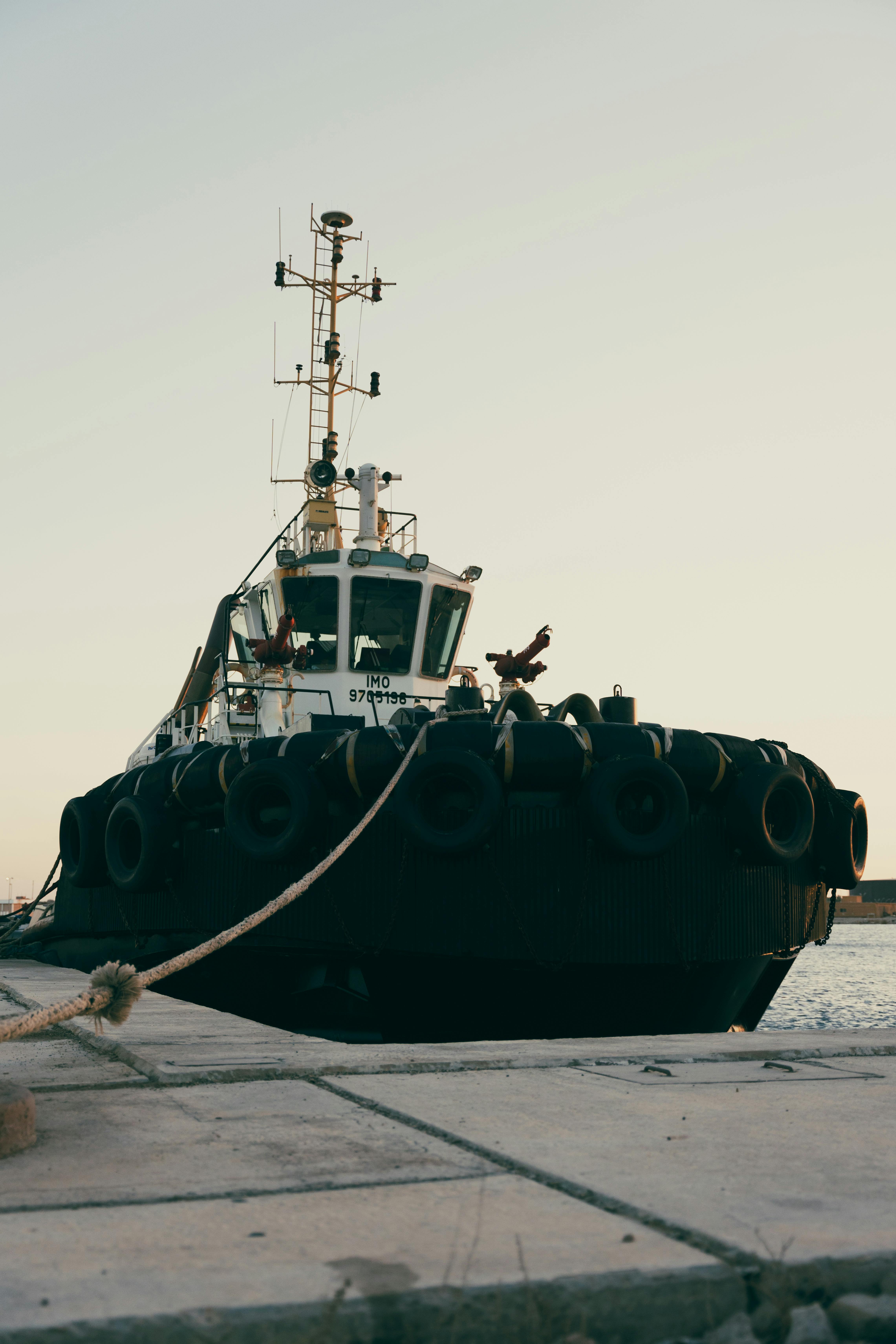ingyenes Egy vontatóhajó biztonságosan kiköt a kikötőben naplementekor, nyugodt tengeri látványt nyújtva. Stockfotó