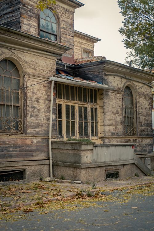 Free A weathered wooden house with arched windows sits quietly in an autumn setting. Stock Photo
