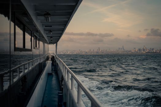 Scenic view of city skyline from a ferry during twilight, showcasing serene ocean waves and urban backdrop.