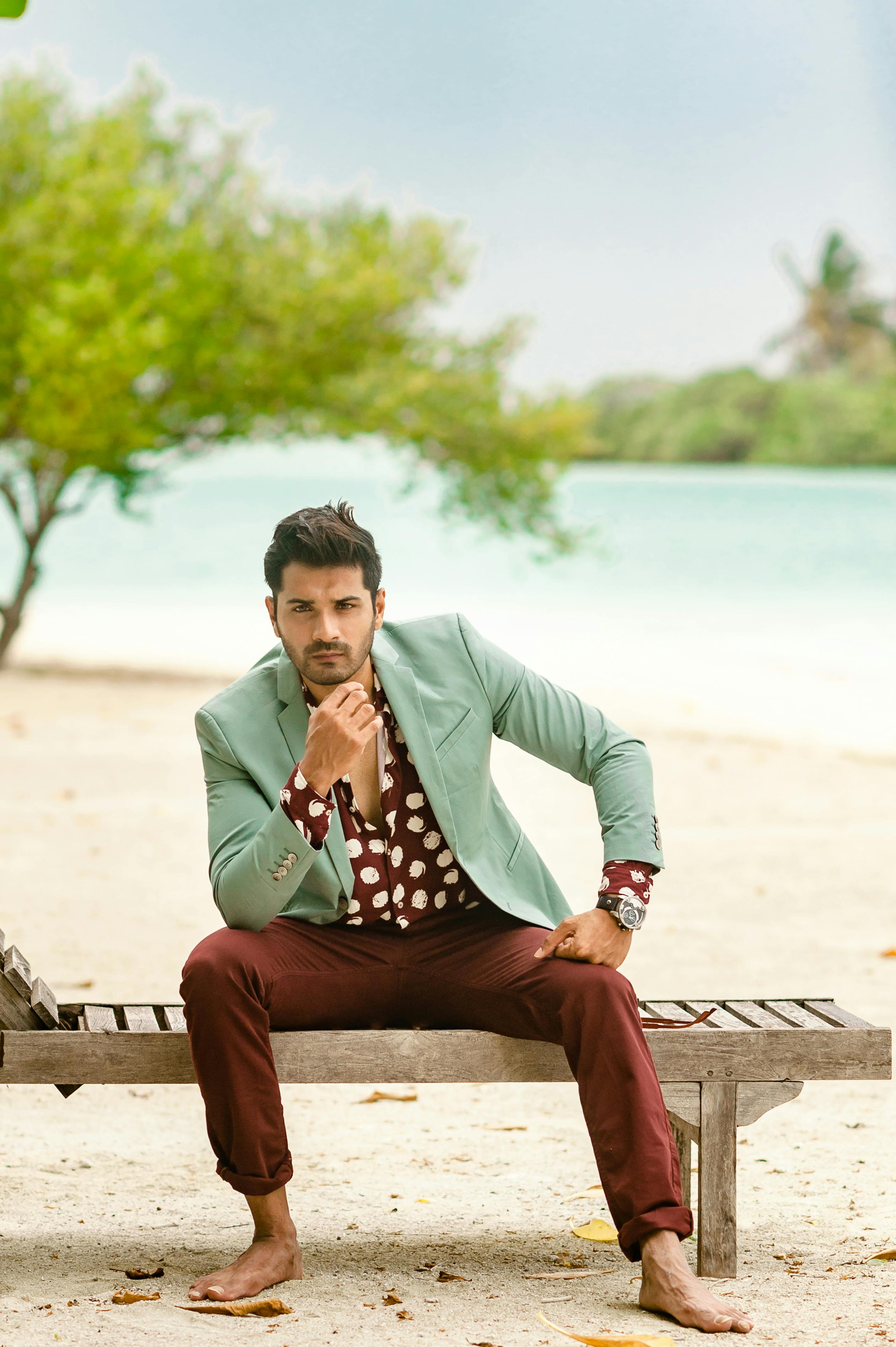 Man in stylish outfit seated on a beach bench in Maldives, embracing tropical style.