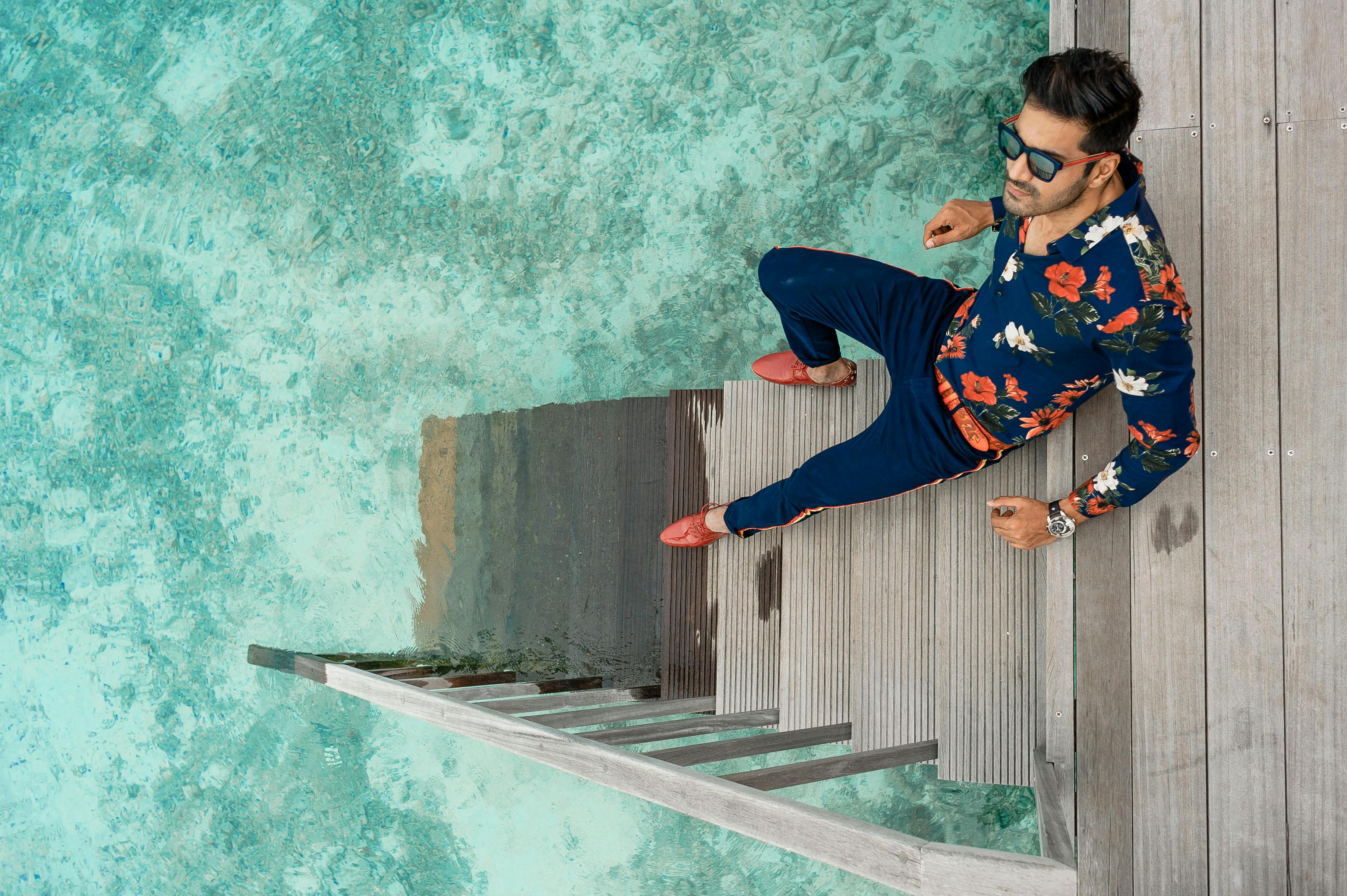 Fashionable man in floral outfit relaxing on stairs over turquoise waters in Maldives.