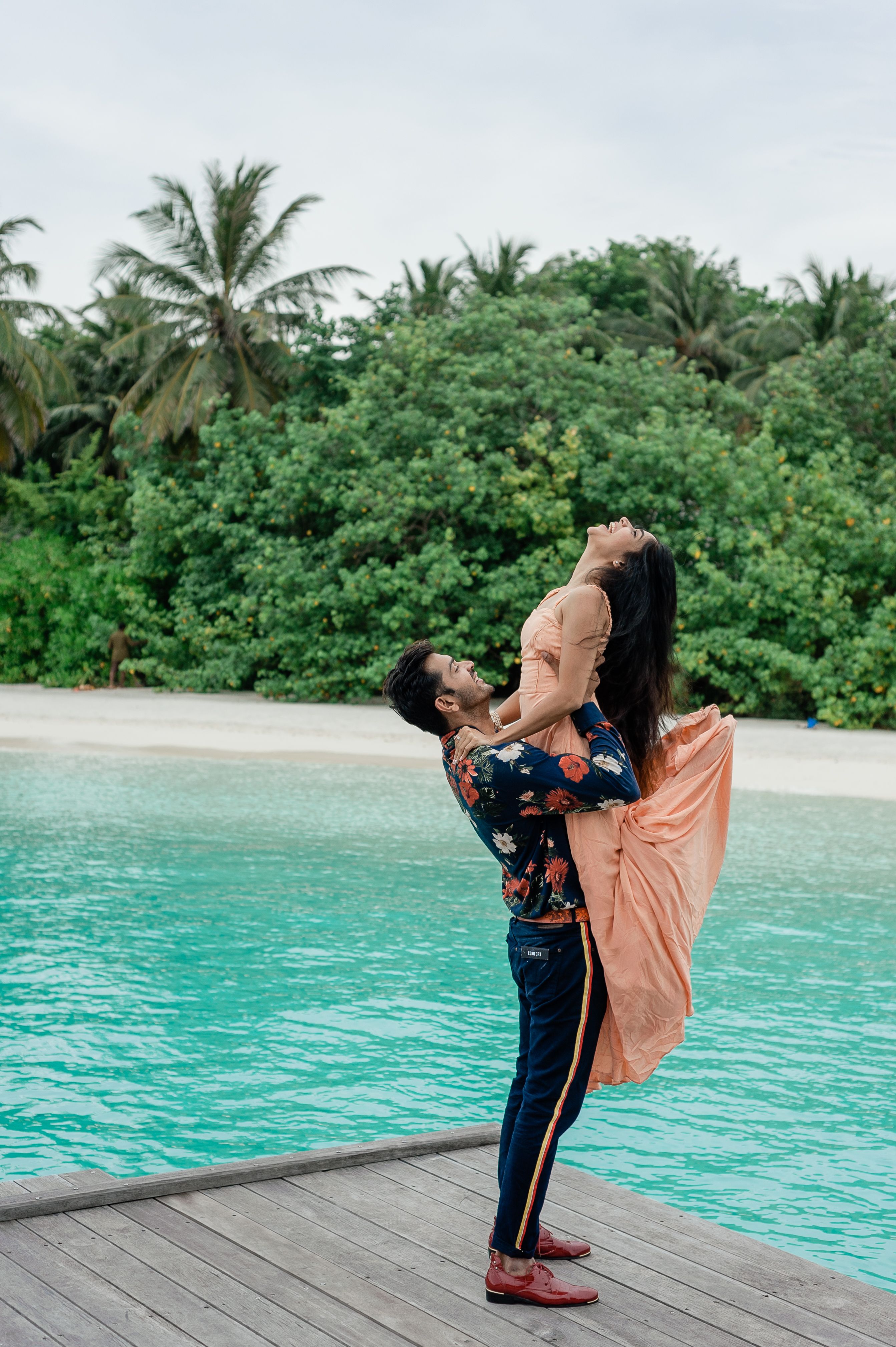 A couple embraces by a serene beach in the Maldives, showcasing island fashion and romance.