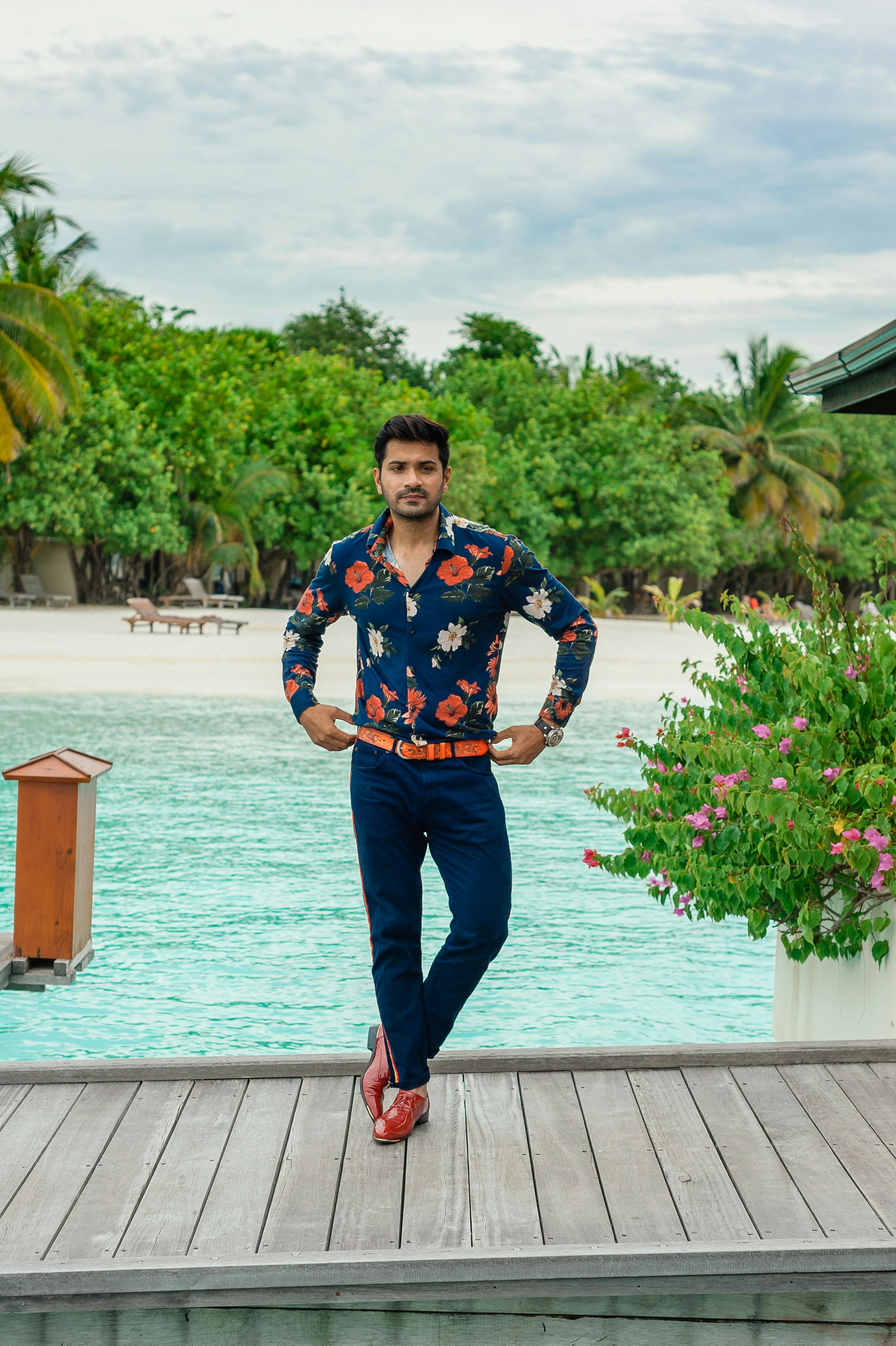 A fashionable man poses near a tropical beach in the Maldives, showcasing casual style.