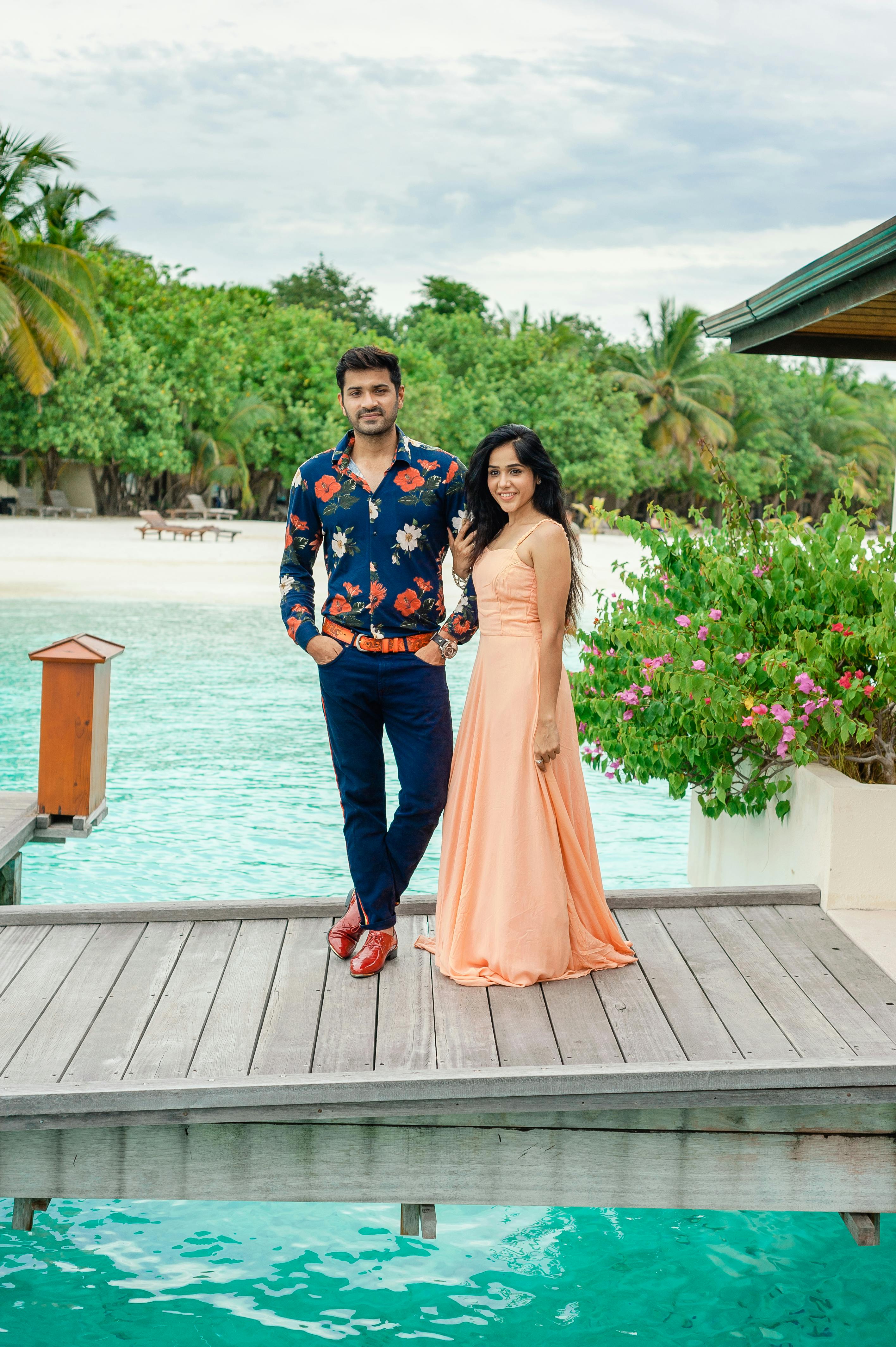 Stylish couple in designer wear by a poolside in a tropical Maldives resort setting.