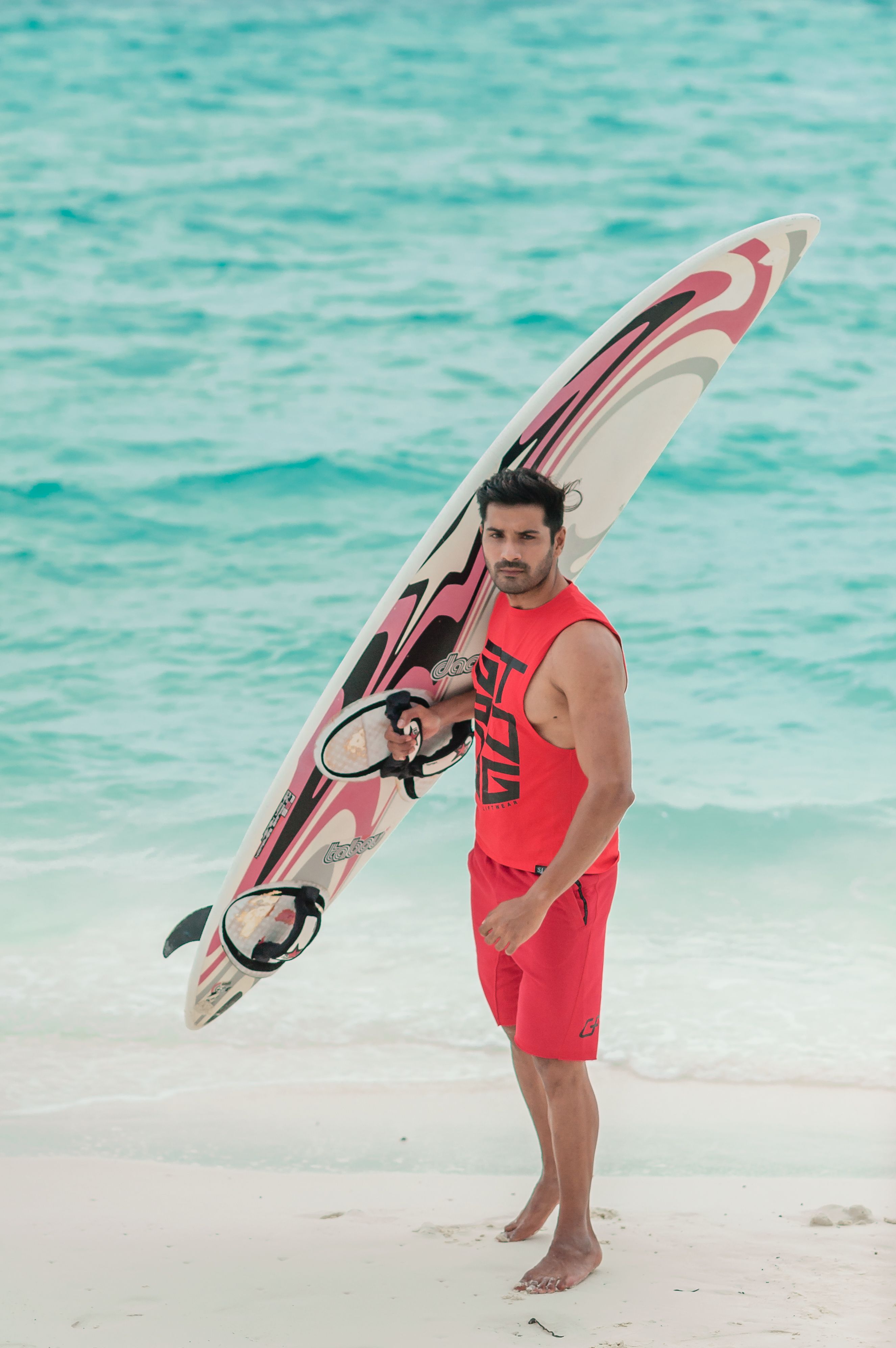 Homem posando com uma prancha de surfe em uma praia das Maldivas em traje de praia da moda.