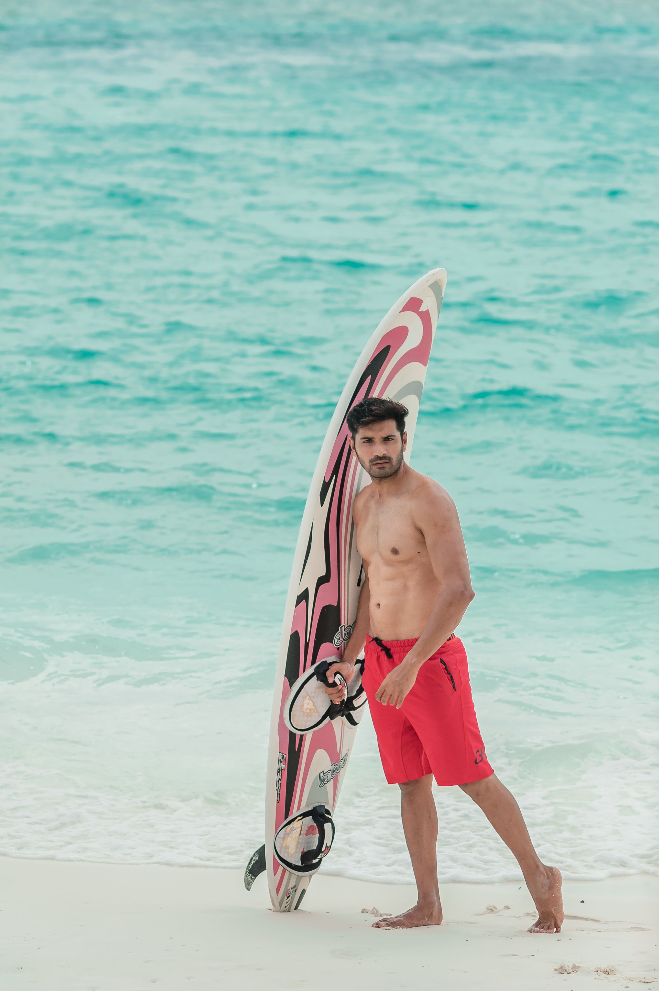 Um homem em pé na praia das Maldivas com uma prancha de surf, abraçando as vibrações tropicais.
