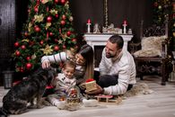 A joyful moment with family by the Christmas tree, gifting and playing with a dog.