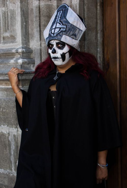 Free Adult in gothic costume with intricate face paint stands against an ornate wall, creating a mysterious atmosphere. Stock Photo