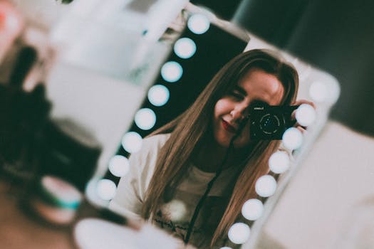 Portrait of a woman with a camera reflected in a lit makeup mirror.