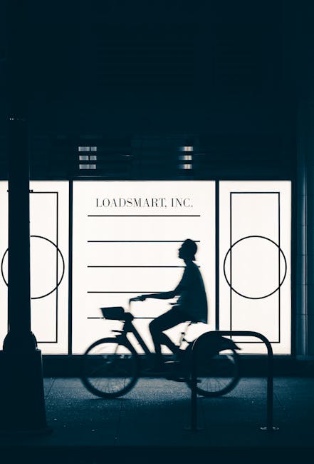 Silhouette of a cyclist riding past an illuminated storefront at night, modern urban scene.