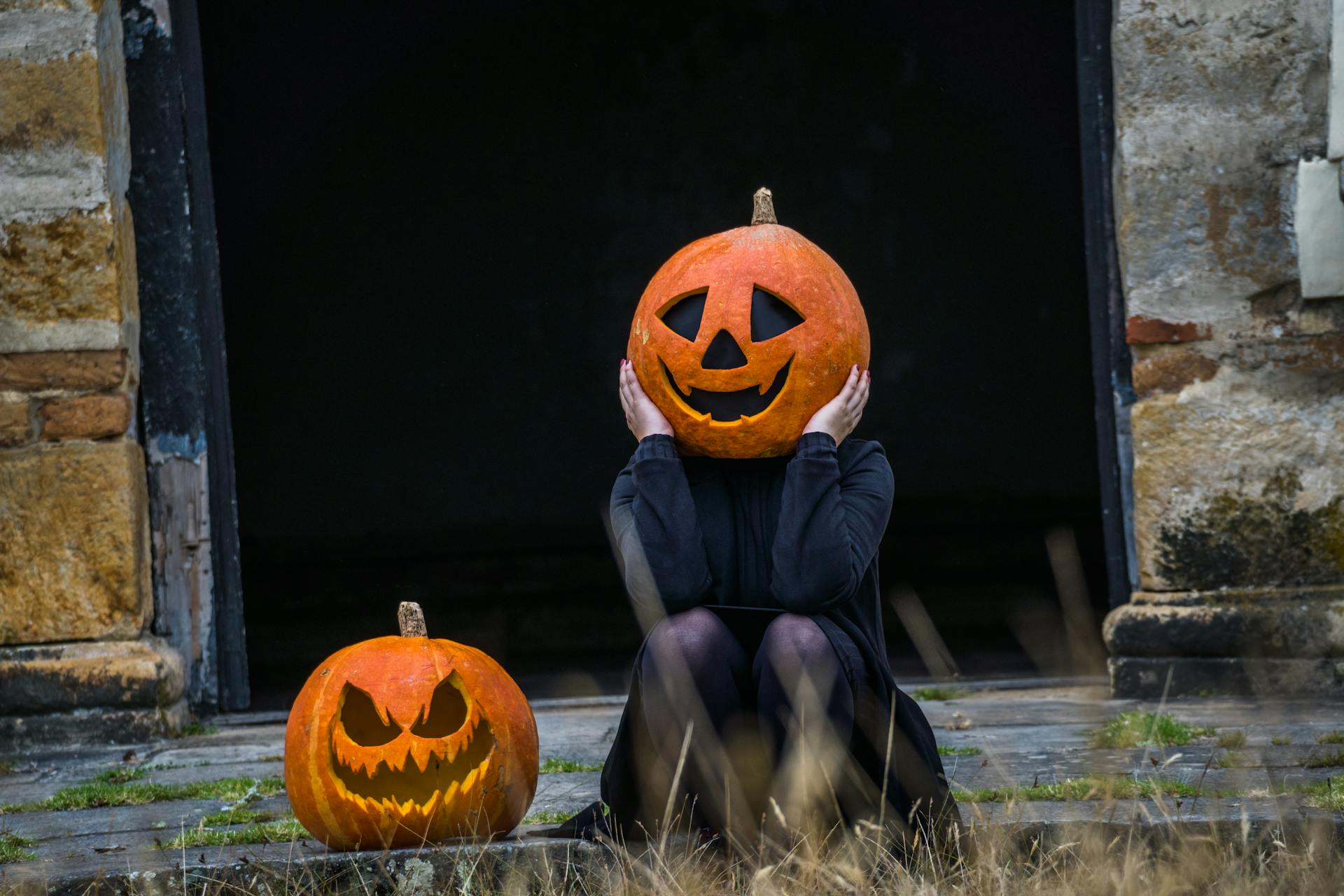 Person with a carved pumpkin head sitting beside another jack-o'-lantern during Halloween night.