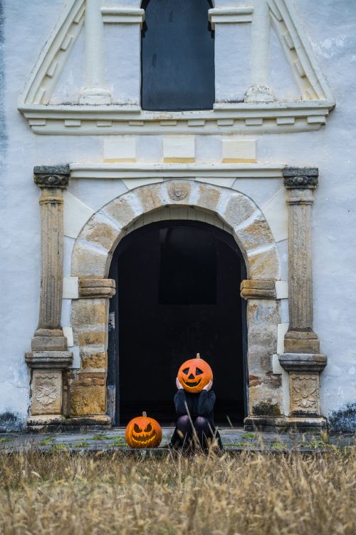 Free A person with a pumpkin head sits outside a historic church in Guasca, Colombia, on a spooky Halloween night. Stock Photo